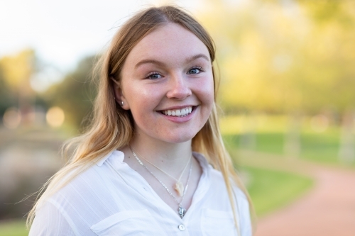 happy teen girl with long blonde hair standing outdoors - Australian Stock Image
