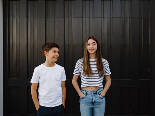 happy teen siblings standing outside against black garage door background - Australian Stock Image