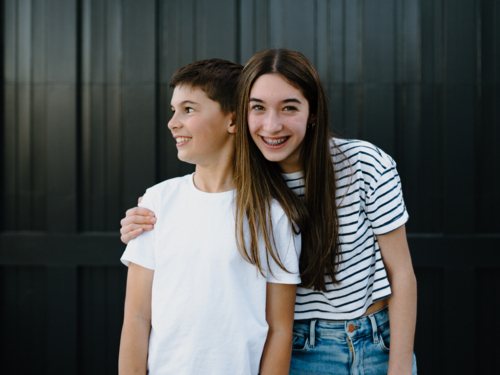 happy teen siblings standing outside against black garage door background - Australian Stock Image