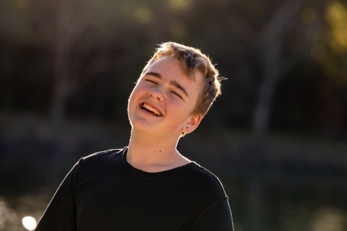 Happy teenage boy by the water in golden afternoon sunshine - Australian Stock Image