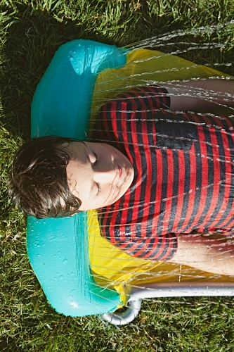 Happy tween boy lying in a sprinkler on a hot summer's day - Australian Stock Image