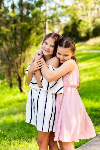 Happy tween sisters hug outside in park