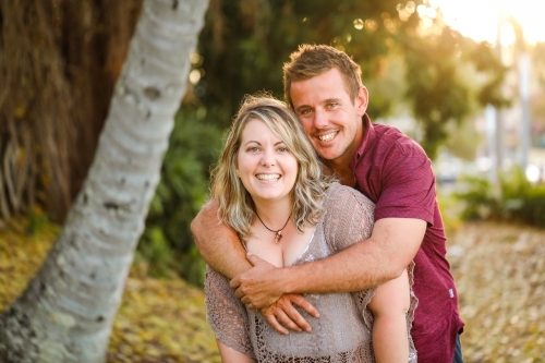 Happy twenty-something couple embracing in golden afternoon light at the park - Australian Stock Image