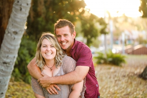 Happy twenty-something couple embracing in golden afternoon light at the park - Australian Stock Image