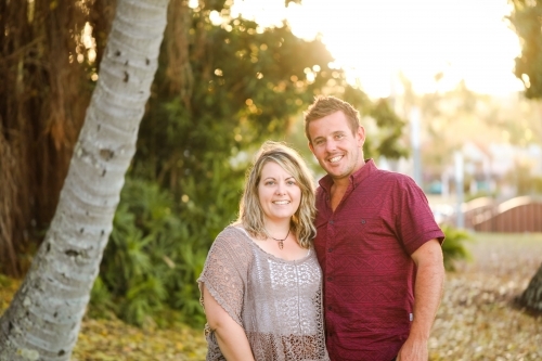 Happy twenty-something couple side hugging in golden afternoon light at the park - Australian Stock Image