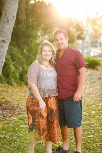 Happy twenty-something couple standing together in golden afternoon light at the park - Australian Stock Image