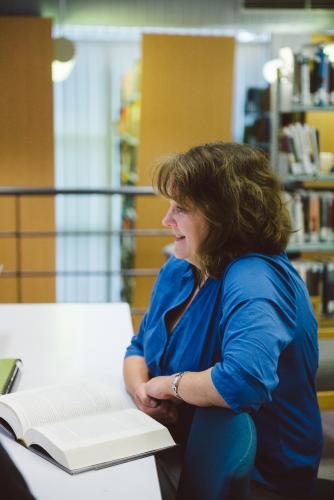 Happy woman reading a book in the university library - Australian Stock Image