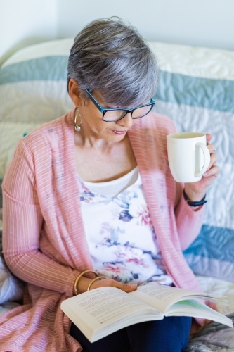 Happy woman reading a book while drinking a cuppa tea - Australian Stock Image