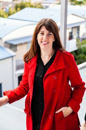 Happy woman standing on balcony in red jacket - Australian Stock Image