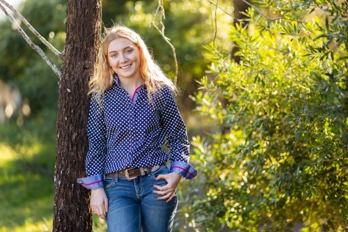 Happy young adult person standing against a tree outside - Australian Stock Image