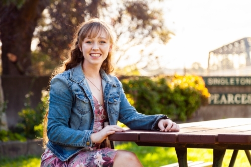 Happy young adult sitting at park bench in autumn - Australian Stock Image