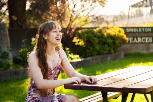 Happy young adult sitting at park bench in autumn - Australian Stock Image