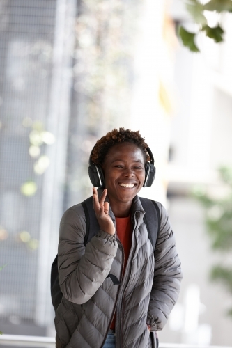 Happy young African woman listening to music wearing wireless headphones in city - Australian Stock Image