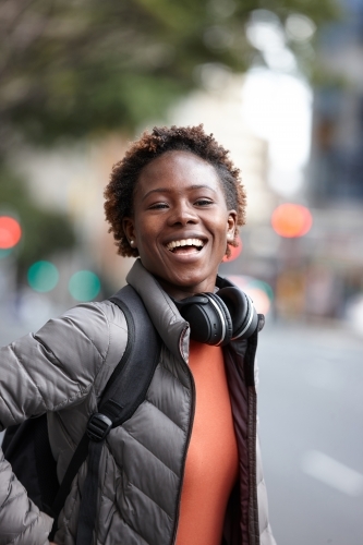 Happy young African woman wearing wireless headphones in city - Australian Stock Image