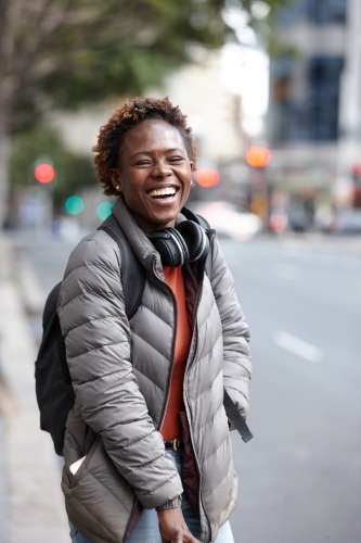 Happy young African woman wearing wireless headphones in city