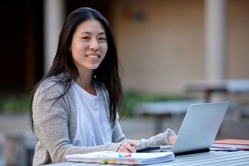 happy Young Asian university student studying on laptop outdoors - Australian Stock Image