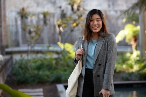 Happy young Asian woman with shopping bag outdoors at enclave - Australian Stock Image