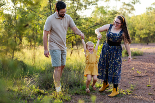Happy young Australian family parents swinging toddler kid together in countryside - Australian Stock Image