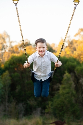 Happy young boy playing on a swing at a park - Australian Stock Image