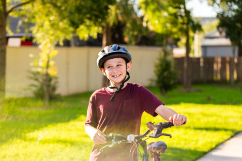 happy young boy with big smile looking to the side while holding bike at park - Australian Stock Image