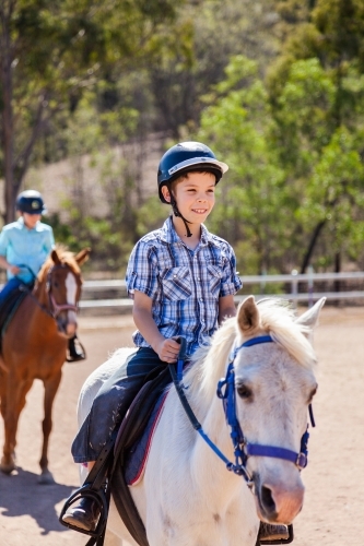 Happy young boy with safety horse riding helmet on horseback during lesson - Australian Stock Image