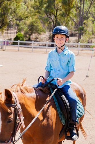 Happy young boy with safety horse riding helmet on horseback during lesson - Australian Stock Image