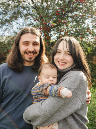 Happy young couple holding baby outside in overgrown garden - Australian Stock Image