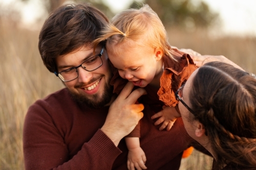 Happy young dad holding toddler girl on shoulder outside at sunset - Australian Stock Image