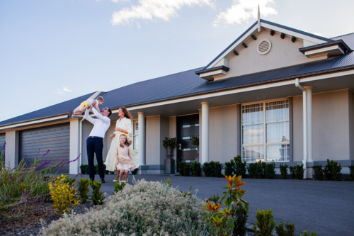 Happy young family outside their large Australian home dad and mum playing with kids on driveway - Australian Stock Image