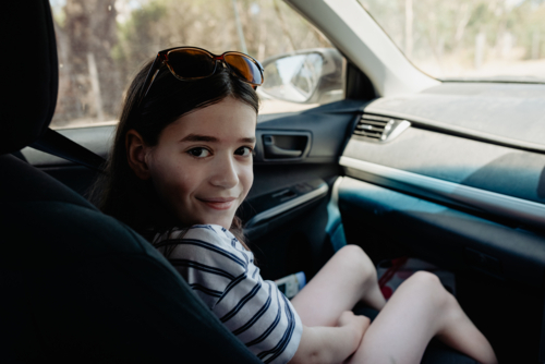 Happy young girl sitting in the front seat of a car looking over her shoulder - Australian Stock Image