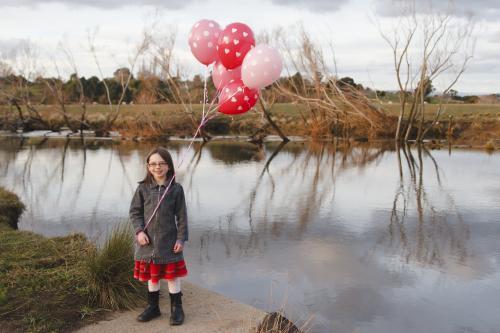Happy young girl with a bunch of birthday pink balloons beside a river - Australian Stock Image
