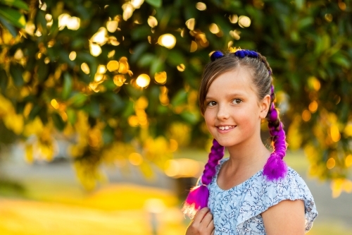 Happy young girl with fun purple braids in hair smiling in warm golden light with copy space - Australian Stock Image