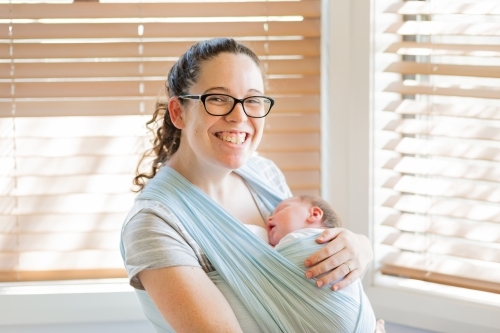 Happy young mother holding her sleeping newborn baby in a wrap sling