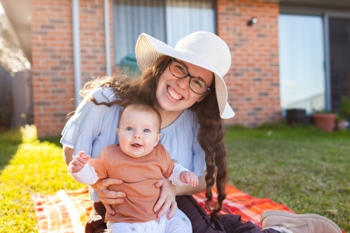 Happy young mum wearing hat outside in winter sun holding happy baby - Australian Stock Image
