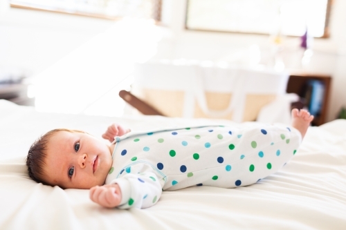 Happy young newborn baby lying on parents bed in bedroom - morning time