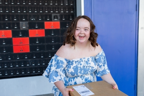 Happy young person with a disability holding brown box parcel near post office - Australian Stock Image