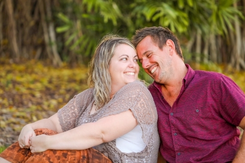 Happy young romantic couple sitting together in golden afternoon light at the park - Australian Stock Image