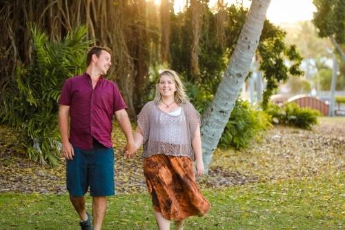 Happy young romantic couple walking together in golden afternoon light at the park - Australian Stock Image