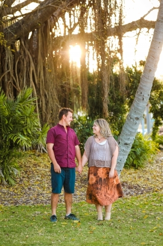 Happy young romantic couple walking together in golden afternoon light at the park - Australian Stock Image