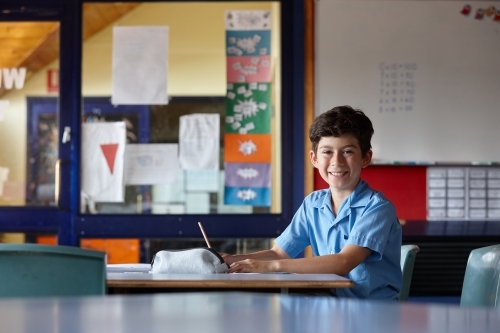 Happy young school boy writing in classroom
