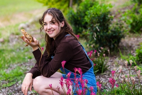 Happy young teen woman with pet bearded dragon lizard in native flower garden - Australian Stock Image