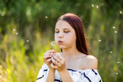 Happy young tween girl outside blowing dandelion flower seeds