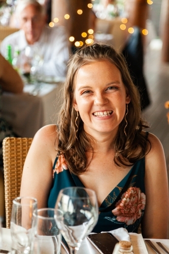 Happy young wedding guest smiling at table during reception - Australian Stock Image