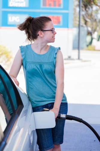 Happy young woman filling up her car with unleaded petrol at the service station - Australian Stock Image