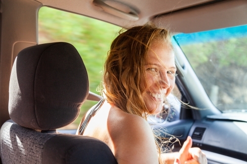 Happy young woman in passenger seat of car coming home from a beach day with friends