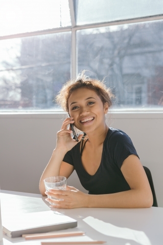 Happy young woman on the phone holding a glass - Australian Stock Image