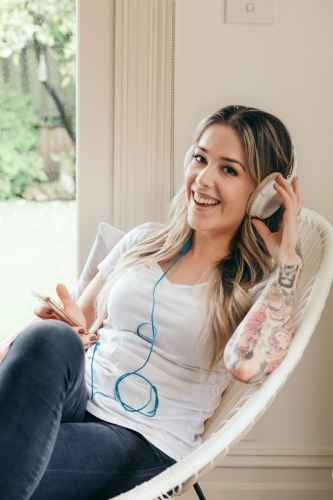 Happy young woman with headphones sitting in lounge chair - Australian Stock Image