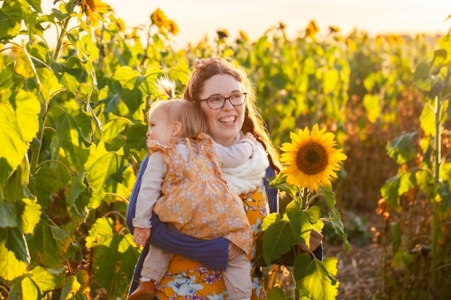 Happy young woman with toddler hugging in sunflower paddock - Australian Stock Image