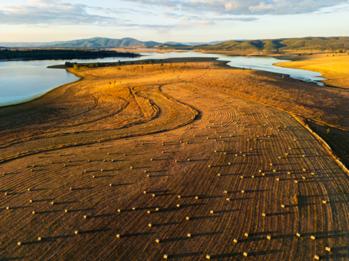 Hay bales dotted in a paddock with Lake Wivenhoe in the background - Australian Stock Image