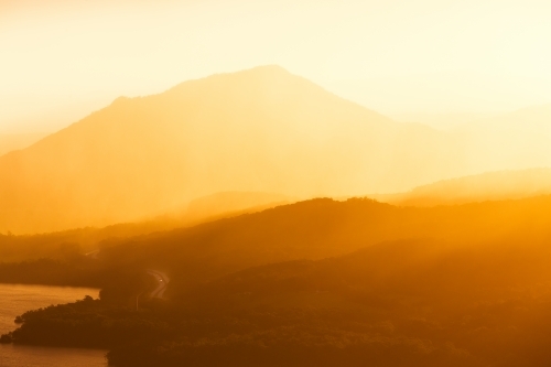 Hazy orange sunset over coastal highway and mountains - Australian Stock Image
